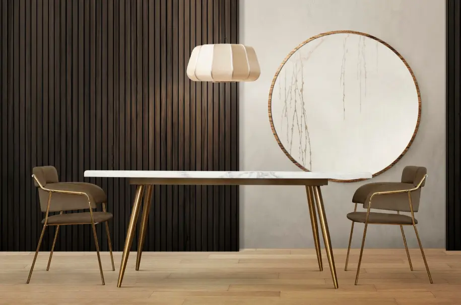 Modern dining table with marble top, gold legs, two upholstered chairs, pendant light, and round wall mirror.