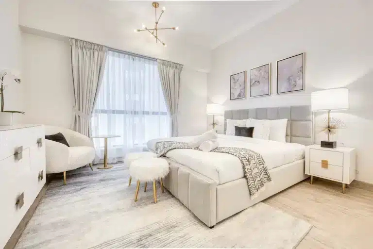 white bedroom with bed, ottoman, side table and armchair