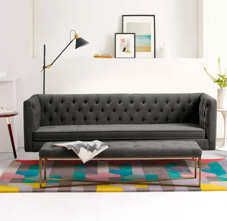 Modern gray tufted sofa paired with a rectangular coffee table on a colorful geometric rug, accented by a floor lamp and wall art.