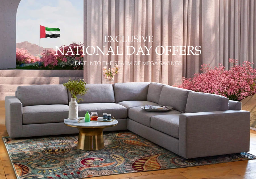 L-shaped gray sofa in a bright room with pink flowers, coffee table, and UAE flag in the background for National Day offers.