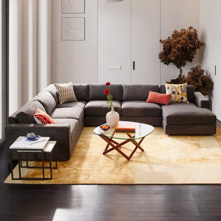 Modern grey sectional sofa with decorative pillows, glass coffee table, and potted plant, enhancing a stylish living room.