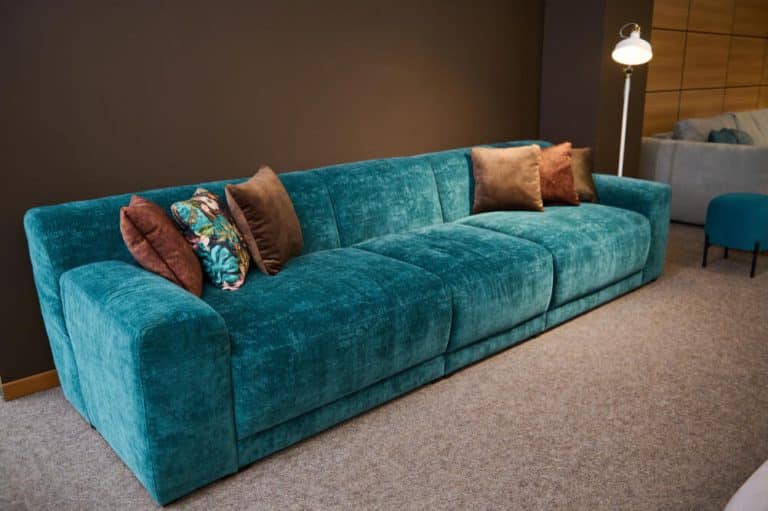 A spacious blue couch positioned in a cozy room, accompanied by a stylish lamp for added ambiance.